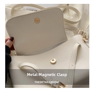 Close-up of golden magnetic buckle on minimalist cream crossbody bag with textured leather