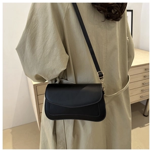 Detail of minimalist black leather crossbody bag with gold buckle on an olive coat