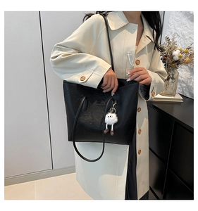 Detail of embossed black tote bag with elegant metallic logo and white plush charm