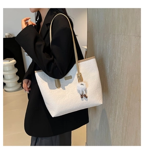 Detail of white embossed tote bag with cartoon patterns and plush toy charm accessory