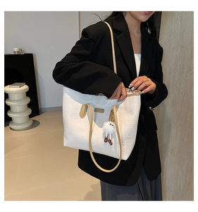 Close-up of white embossed tote bag with cartoon bear pattern and plush ball charm