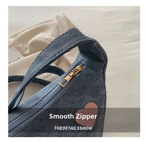 Detailed close-up of smooth gold metal zipper and heart leather patch on blue denim bag