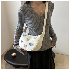 Close-up of beige crescent bag with colorful leather heart patches and long shoulder strap
