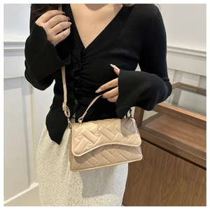Detail of beige quilted handbag with woven texture held by model in elegant outfit