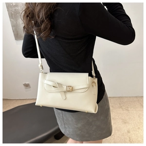 Detail of a cream faux leather shoulder bag with a buckle strap on a female model