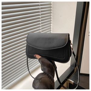Close-up of minimalist black leather square bag with gold hardware and fine stitching
