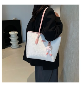 Detail of white embossed tote bag with pink handles and cute monster charm accessory