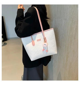 Detail of white embossed tote bag with pink trim and cute plush charm on a model