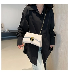 Détail d'un sac carré beige élégant avec fermoir doré en T et bandoulière chaîne