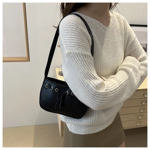 Detail of black matte leather shoulder bag with gold metal eyelets and drawstring accents