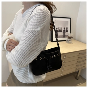 Black leather shoulder bag with drawstring detail shown on model in white knit sweater