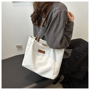 Detail of white tote bag featuring brown leather straps and elegant metal chain link