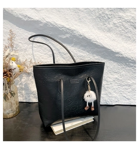 Detail of black PU leather tote with embossed cartoon patterns and white plush charm