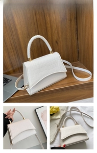 Detail of white crocodile pattern handbag featuring woven handles and gold hardware