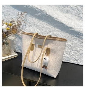 Detail of beige tote bag showing embossed cartoon motifs and plush ball pendant charm