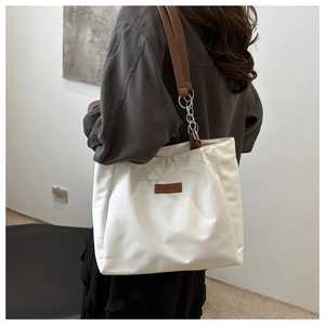 Detail of white canvas tote bag with brown leather strap and chain on model shoulder