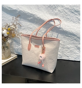 Detail of cream tote bag with cartoon embossing and a pink furry doll charm hanging