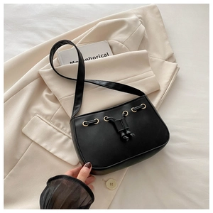 Detail of black faux leather shoulder bag with gold metal eyelets and drawstring decor