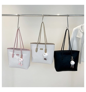 Three commuter tote bags with cartoon embossing and plush charms on a display rack