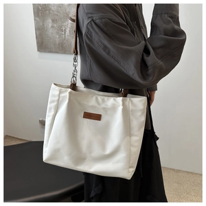 Detail of white tote bag with brown leather strap and silver chain accent for commute