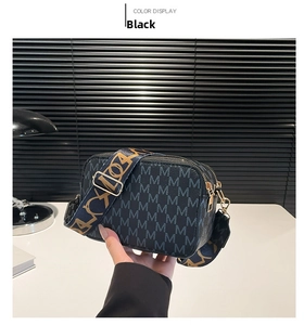 Detail of black crossbody bag featuring grey monogram print and wide woven shoulder strap