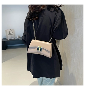 Détail du sac à bandoulière beige clair avec boucle en T dorée sur le rabat en cuir lisse