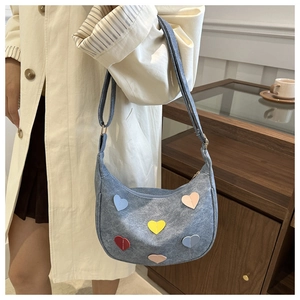 Detail of grey crescent shoulder bag with colorful heart patches on a beige trench coat