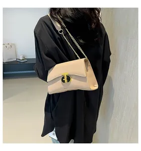 Détail du sac à rabat beige avec serrure en T dorée et bandoulière sur chemise noire