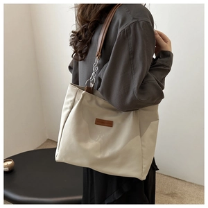 Detail of beige nylon tote bag featuring brown leather straps and silver chain accents