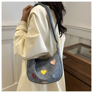 Detail of grey canvas hobo bag with four colorful heart patches worn with a trench coat