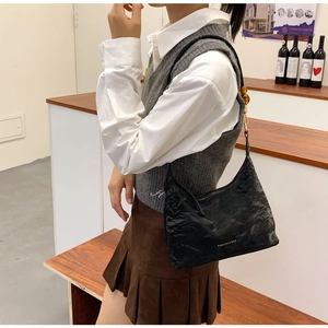 Detail of black pleated faux leather shoulder bag with amber beads and gold lettering