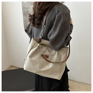 Detail of off-white tote bag featuring brown leather handles and decorative silver chains