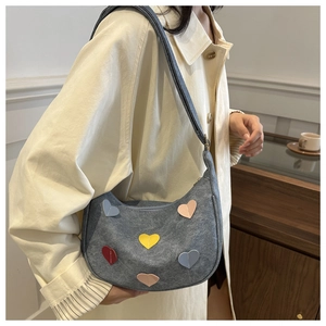 Detail of grey denim crescent bag featuring colorful heart patches and adjustable strap