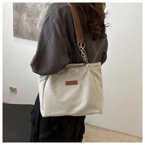 Detail of off-white tote bag showing wide brown strap and Fashion & Budai logo tag