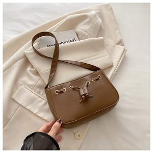 Detail of brown faux leather shoulder bag with drawstring accents and gold metal eyelets