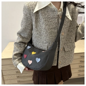 Detail of grey crescent shoulder bag featuring colorful heart patches and wide strap