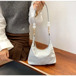 Detail of silver pleated handbag featuring chunky white pearl strap and gold hardware