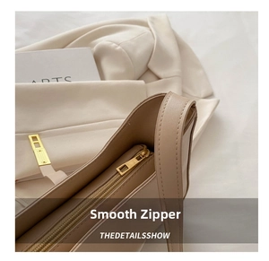 Close-up of the smooth golden metal zipper and beige faux leather on the shoulder bag