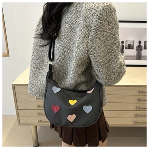 Detail of a black half-moon shoulder bag with colorful heart patches worn by a model