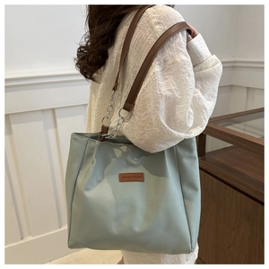 Side view of large mint green tote bag with brown leather strap and chain on a model