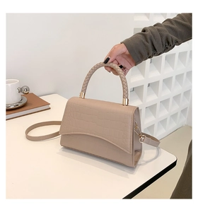 Detail of beige faux crocodile leather bag with woven handle and elegant wavy flap design