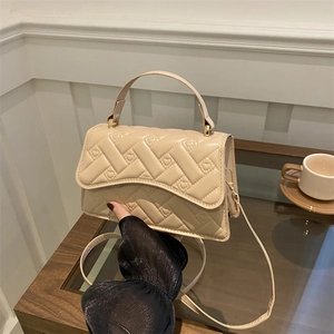 Beige quilted handbag with heart pattern embroidery and gold hardware on a wooden table