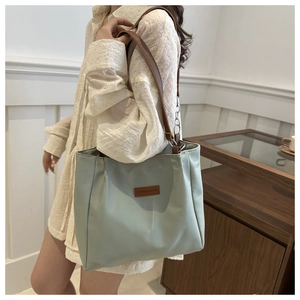 Detailed view of mint green nylon tote bag with brown leather strap worn by a model