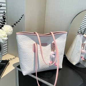 Off-white embossed tote bag with pink straps and plush charm in a lifestyle setting