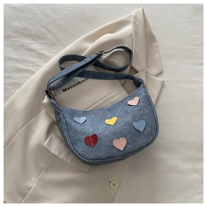 Detailed close-up of blue denim crescent bag with colorful heart-shaped patchwork decor
