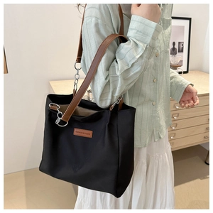 Detail of black tote bag featuring brown leather logo patch and silver chain strap details