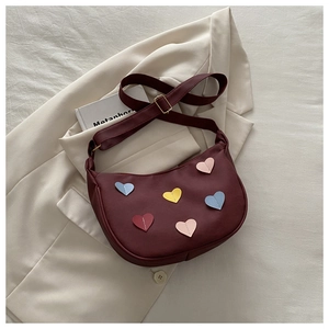 Detail of burgundy crescent bag featuring colorful heart patches and adjustable strap