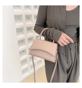 Detail of beige crocodile pattern handbag featuring a woven handle and gold hardware