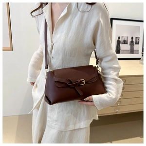 Detail of dark brown leather crossbody bag with bow buckle and gold hardware worn by model