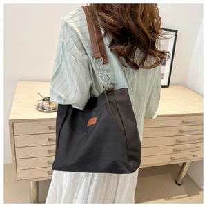Detail of black canvas tote bag with brown leather strap and silver chain linkage